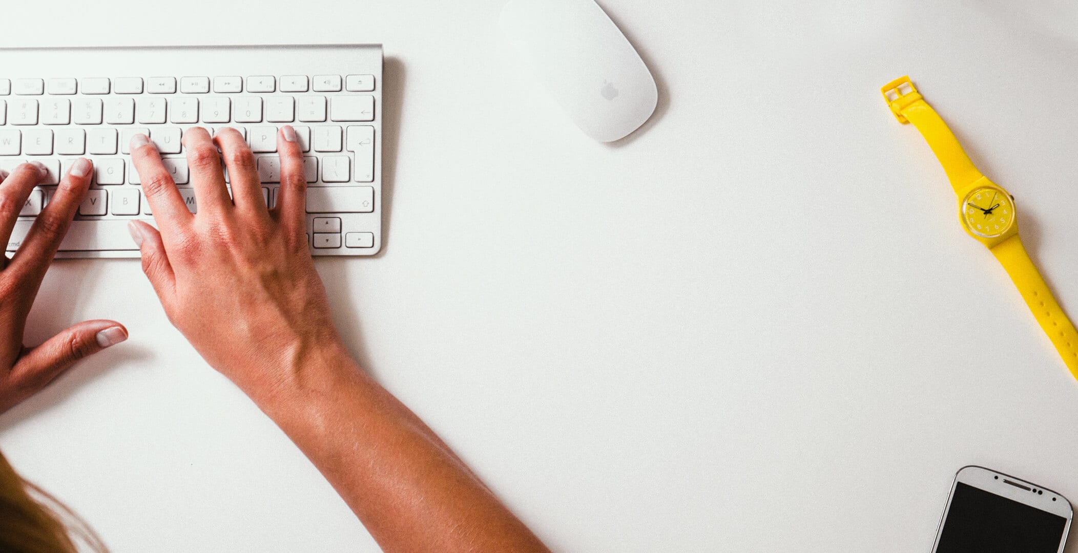 left side: Person typing on slim keyboard, right side, mouse, watch and smart phone.