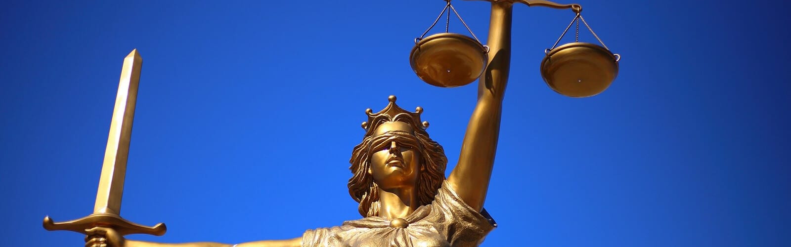 Image of Blind Justice Statue - blindfolded woman wearing crown, sword in one hand, scale in the other.
