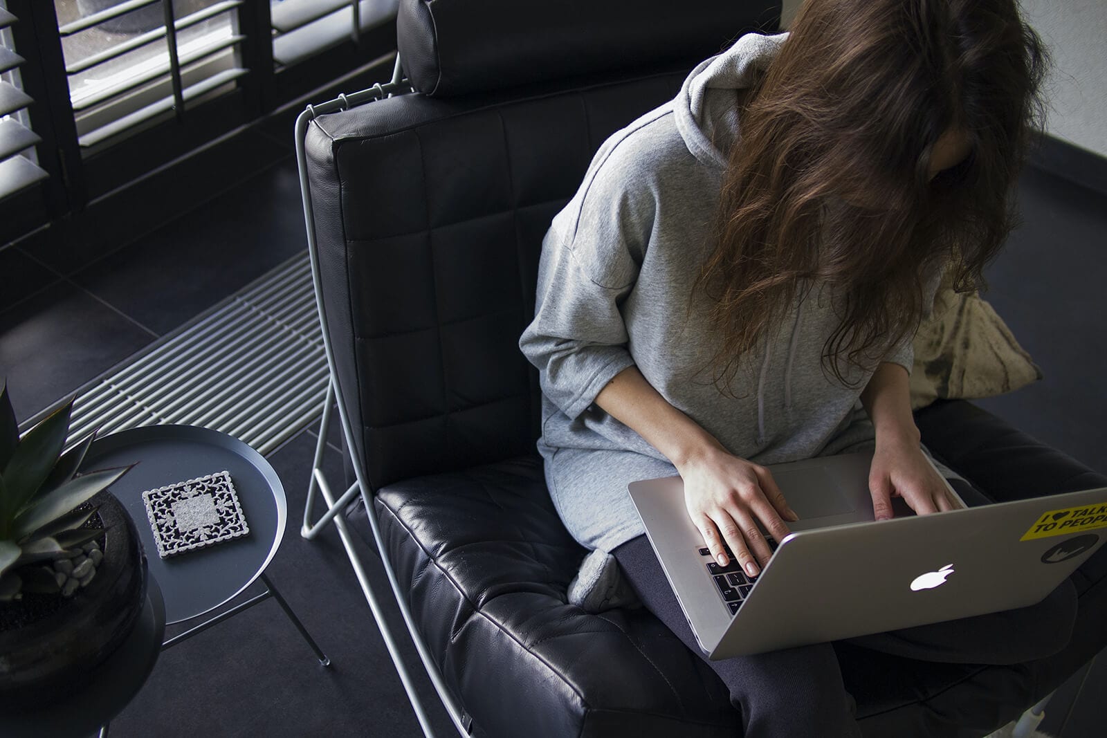 Woman sitting in black leather chair working on Apple laptop computer.