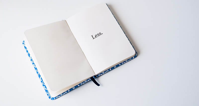 Blue and white open notebook with the word 'Less' on a white countertop.