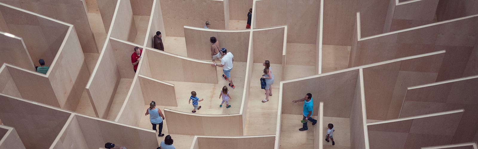 Human sized wooden maze with people of different ages walking through.