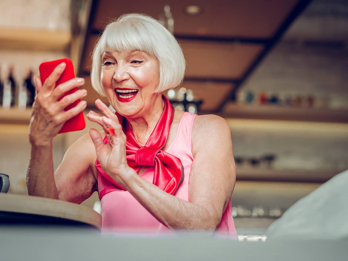 Happy woman from the Boomer Generation smiling holding a smart phone in a restaurant