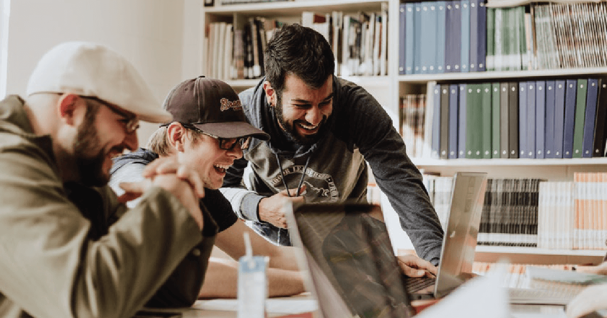 3 males laughing looking at a laptop screen