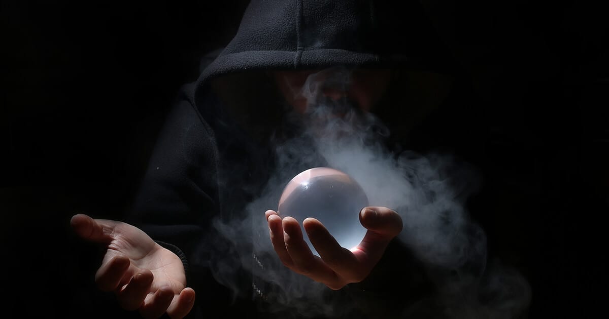 black background with black hooded & shadowed person holding crystal ball