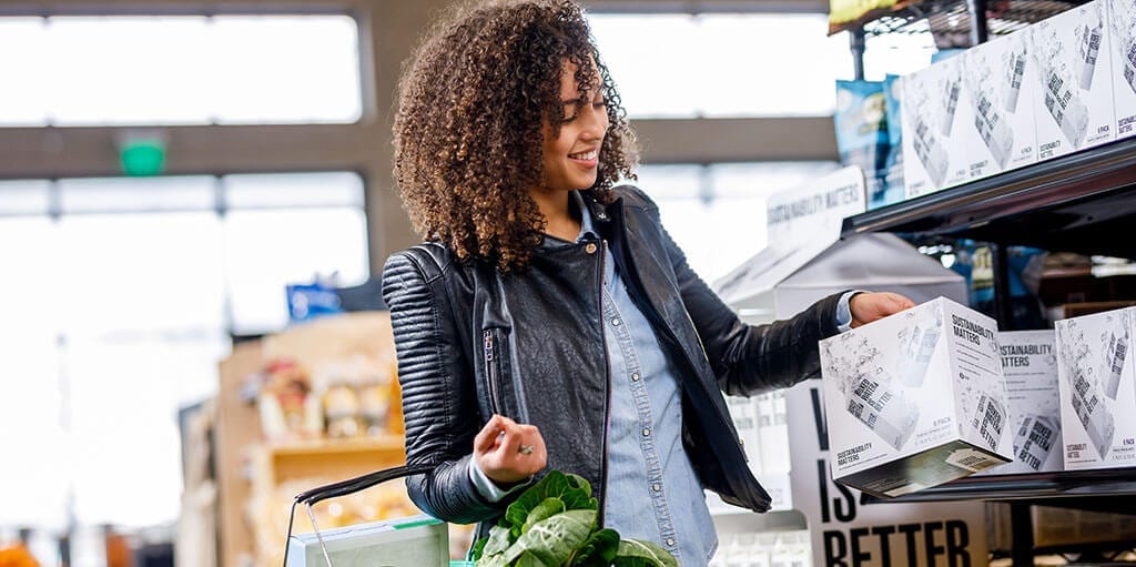 woman picking up a box of water in a supermarket with a shopping basket on her arm