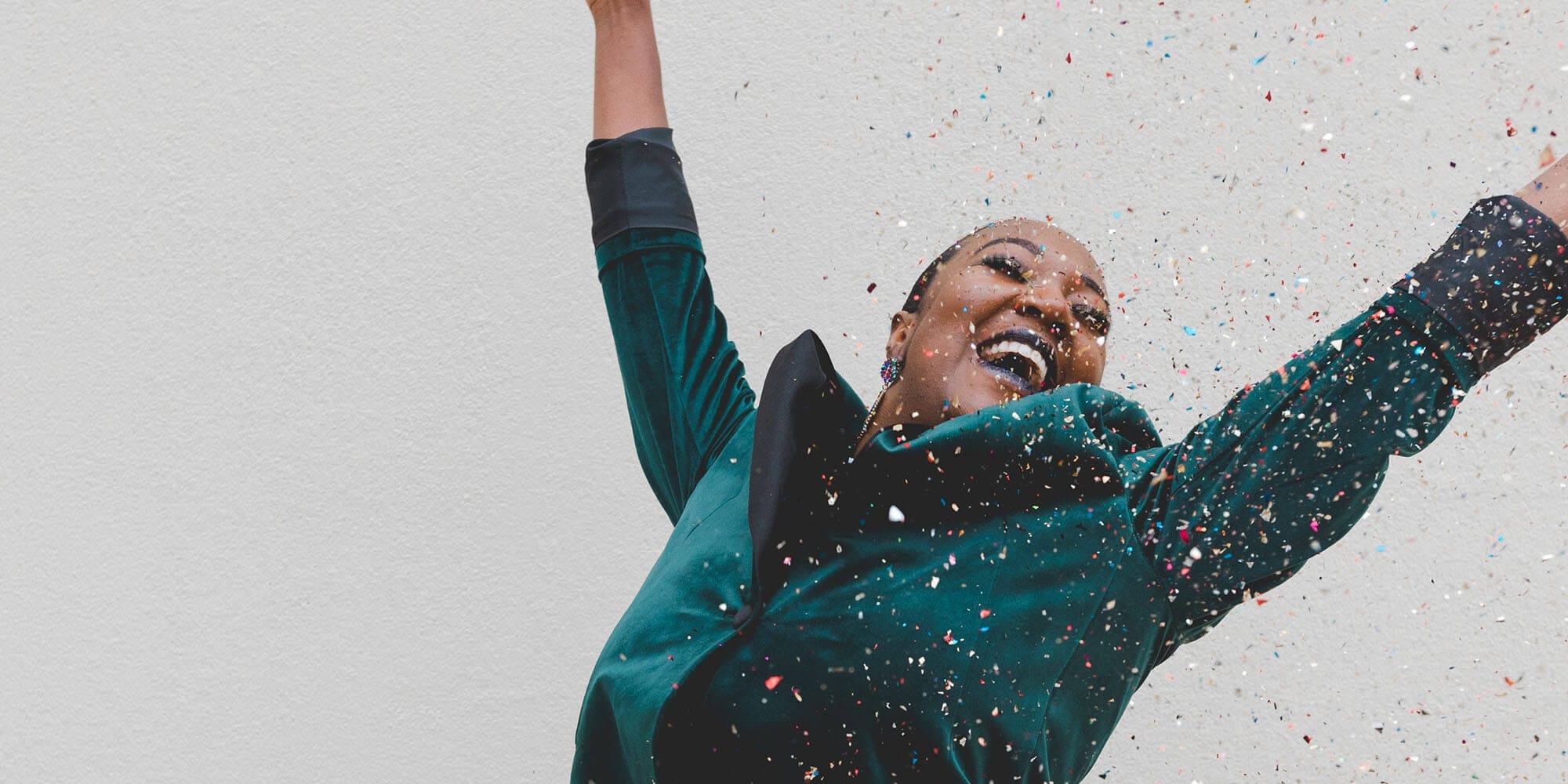 Woman in green jacket, hands up in celebration and multi-colored confetti falling.