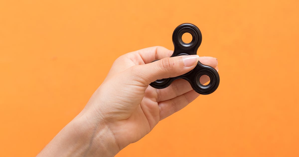 orange background, hand holding a fidget spinner toy.