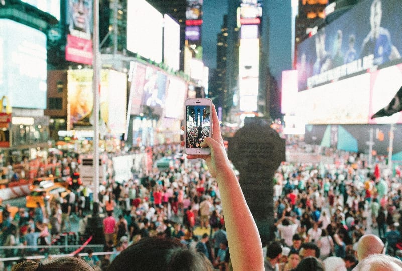Person taking a social video of a street full of people.