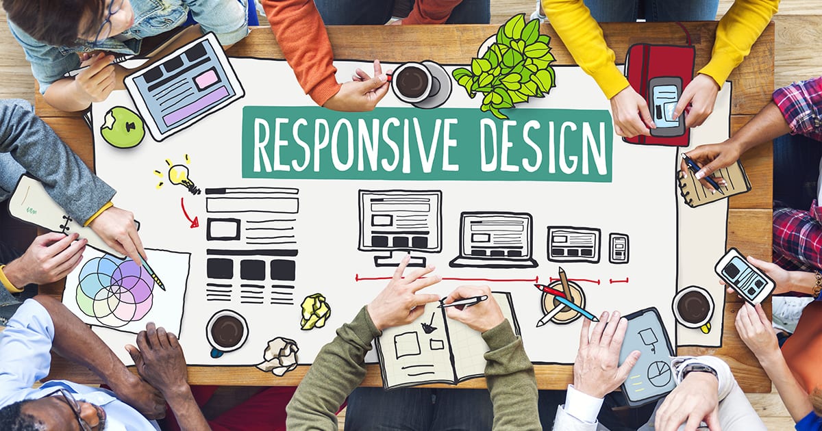 looking down from above on People working at a desk together. Text in the middle of the desk says "Responsive design" and has mockup drawings below.