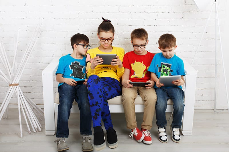 Children sitting on a couch while staring at iPads