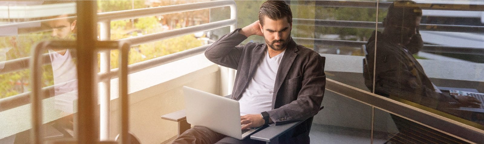 Frustrated male sitting on balcony working on laptop computer