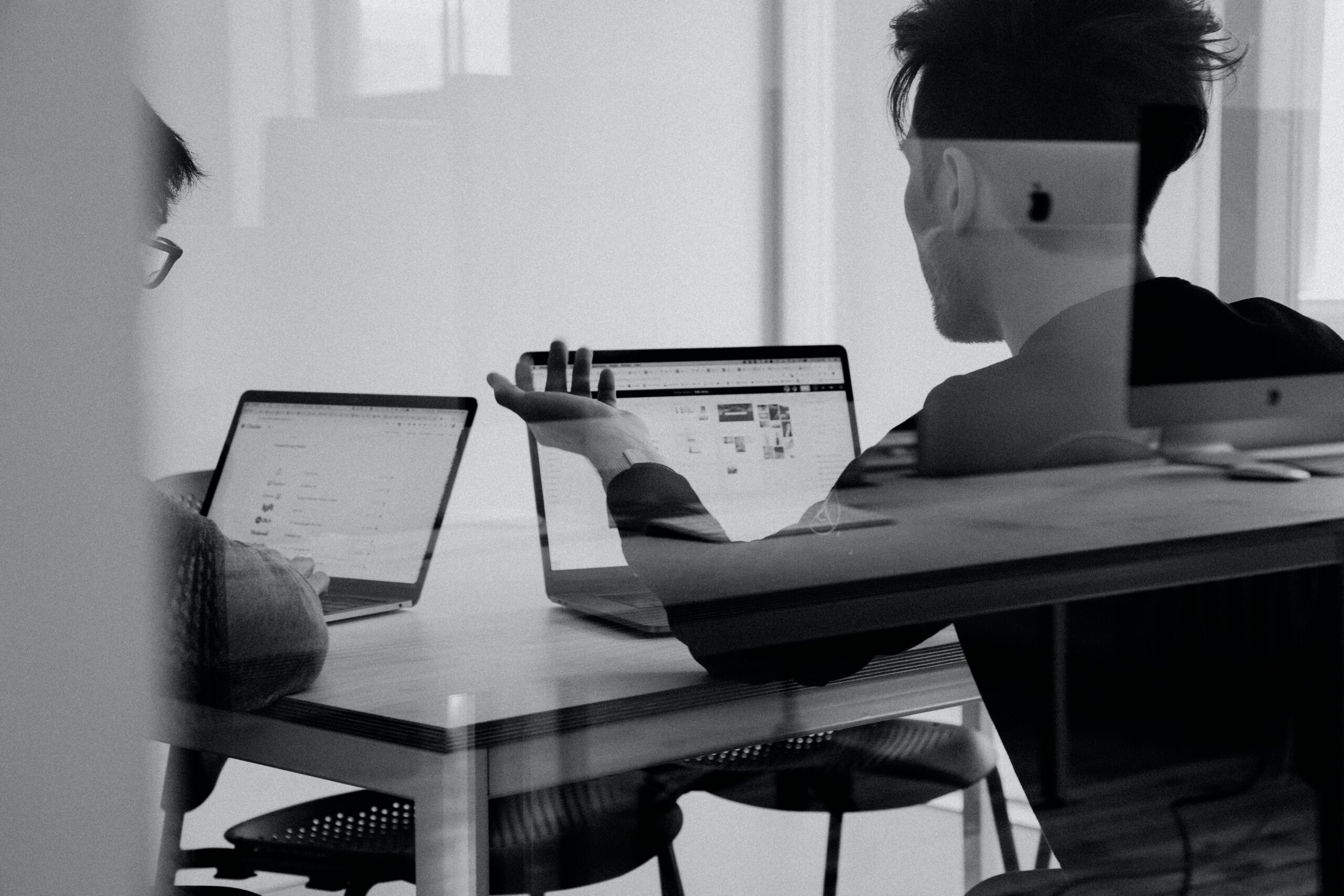 Black and white of men working in office on laptop computers having a discussion