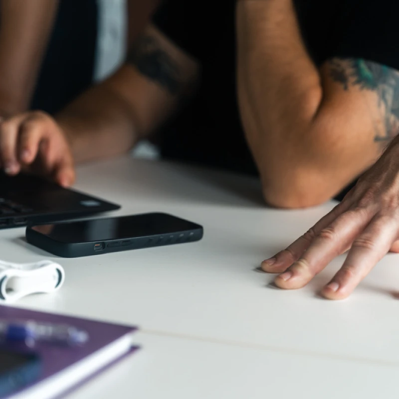 Hand leaning on table with phone and laptop in the background