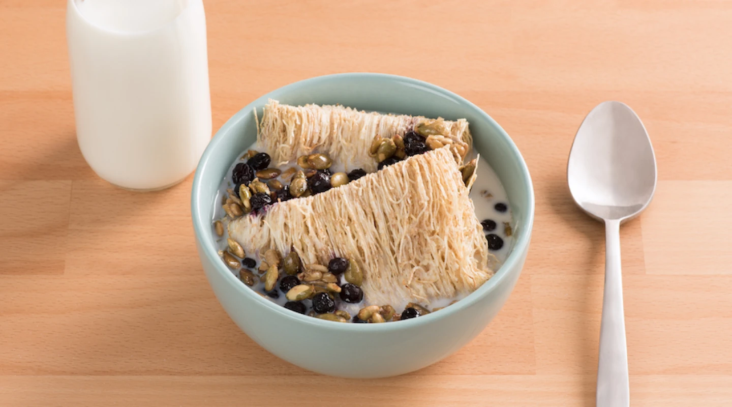 Bowl of shredded wheat with a spoon and bottle of milk beside it on a wooden table